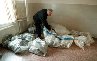 Montgomery County coroner Ed Rovere examines a body at the Rockville Adult Learning Annex, where RIF extremists killed 52 illiterates with a pipe bomb Friday. Experts say reading-is-fundamentalism is a growing movement in the U.S.